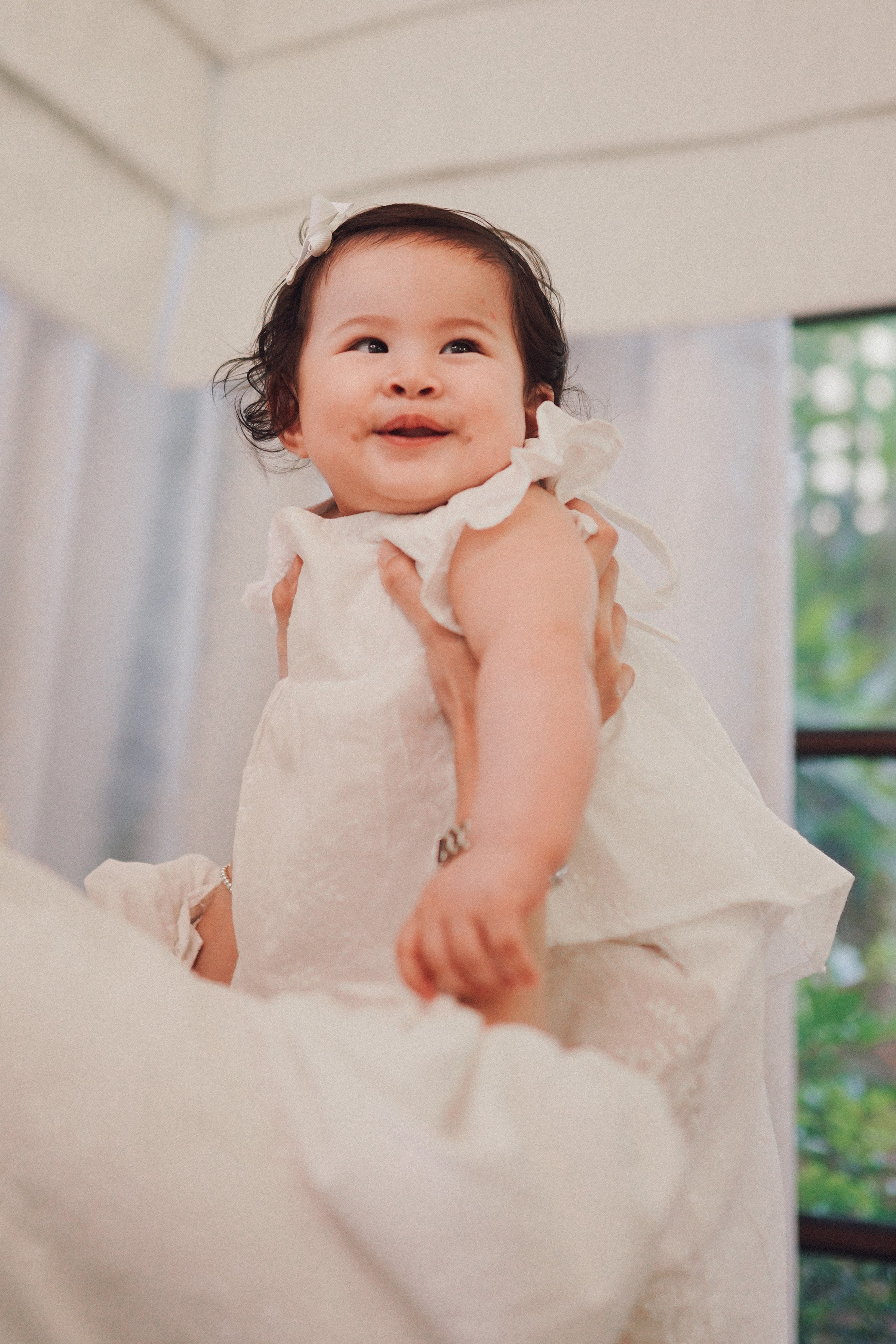 Little baby wearing a white dress and being held by her mother