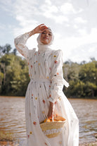 female model in modest gown made by petit moi. holding a basket of oranges