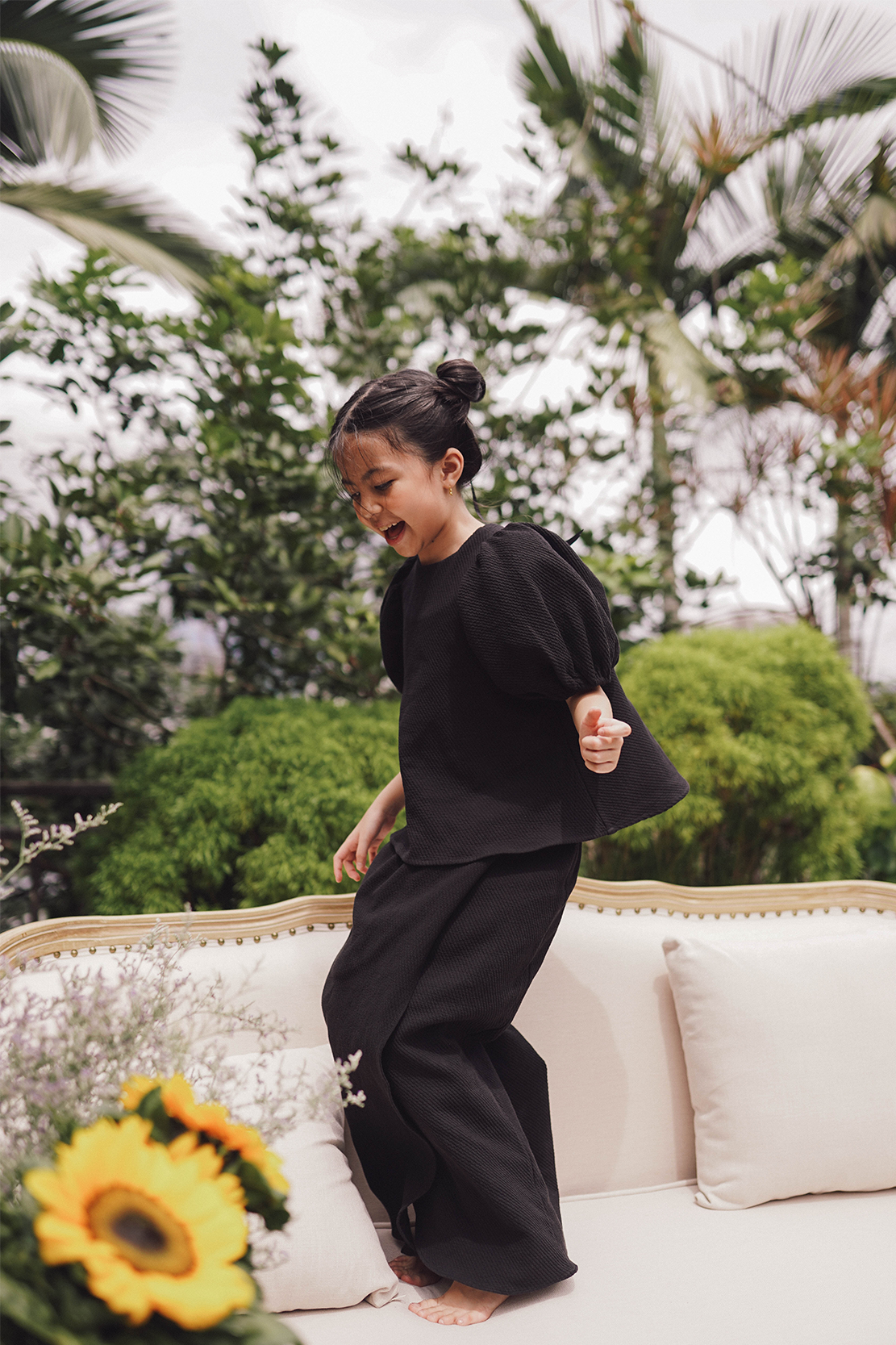 little girl in black baju kurung made by petit moi jumping on the sofa