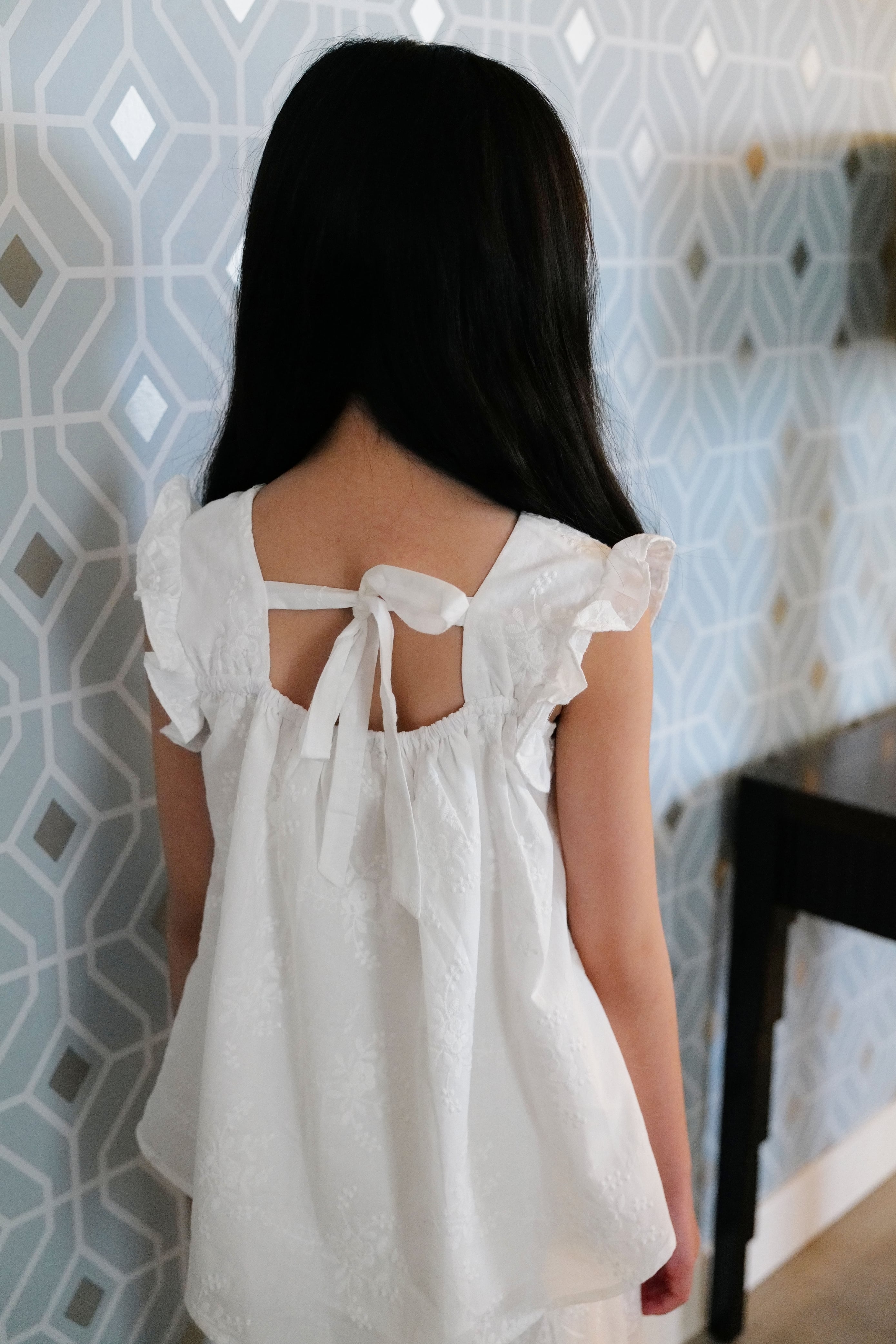 Little girl wearing a white dress facing a blue wall