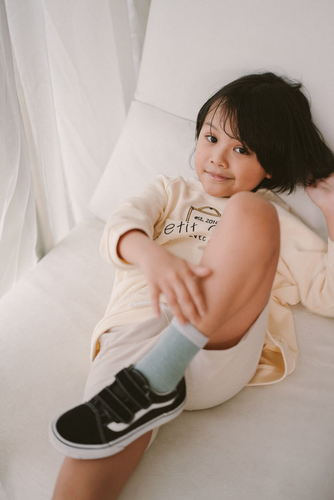 little kid lying down and posing for the camera. wearing high quality sweater by petit moi