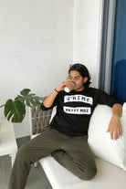 Male model in high quality black sweater by petit moi. Drinking a cup of coffee on a couch
