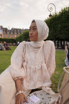 Female model sitting down in a park in paris. While wearing a high quality french inspired top by petit moi