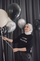 Female model in high quality black sweater made by petit moi. Holding balloons and posing for the camera