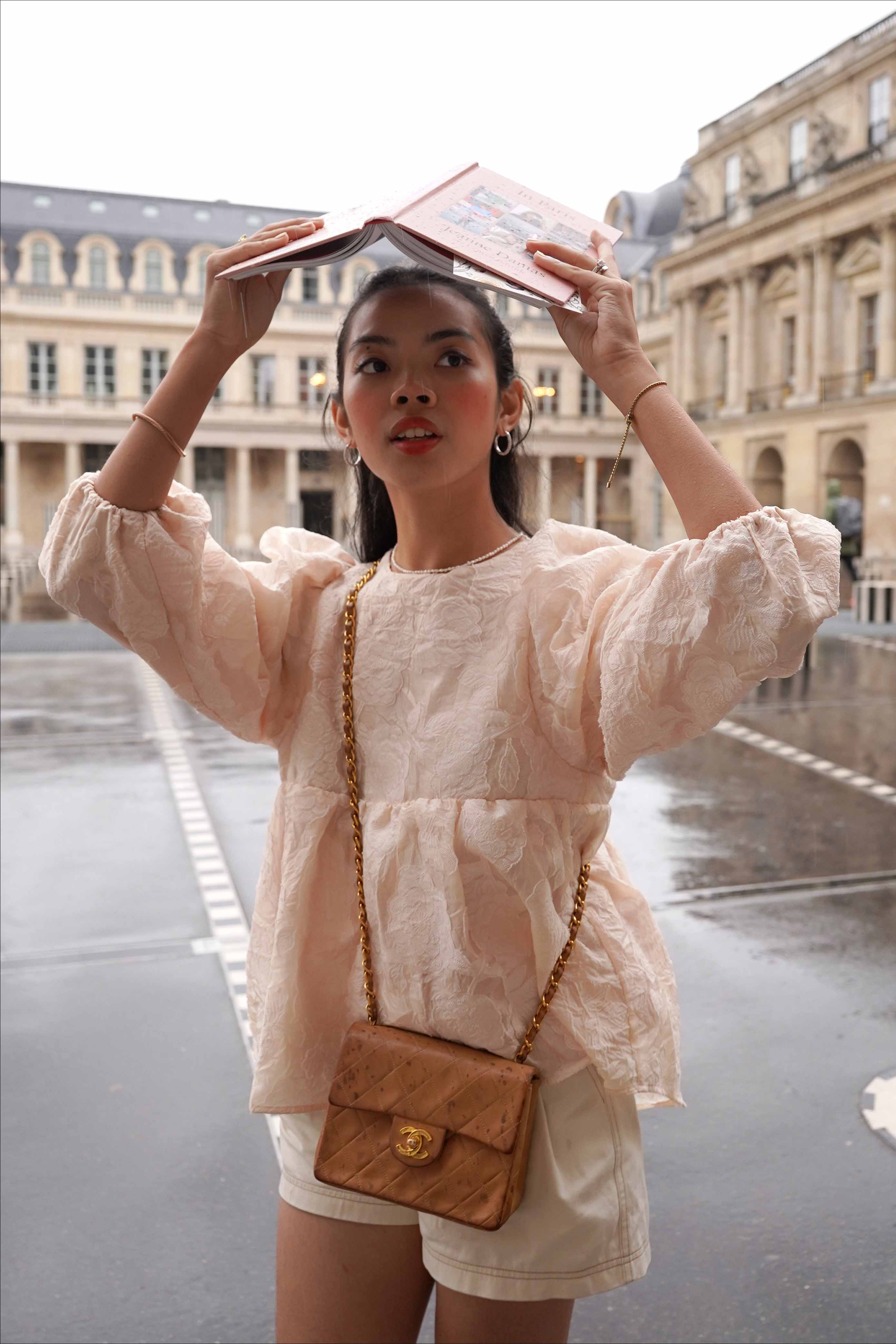 Female model holding book over her head to cover herself from the rain. Wearing french inspired top made by petit moi