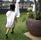 Little girl in garden wearing a white dress made by petit moi