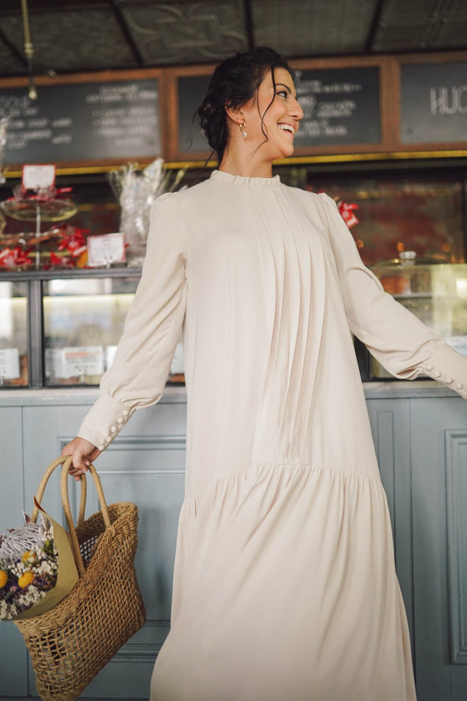 female model wearing a high quality cream dress made by petit moi. posing in the cafe