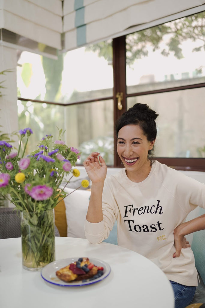 Woman in high quality sweater made by petit moi. Sitting down at a table with flowers and her favourite dish