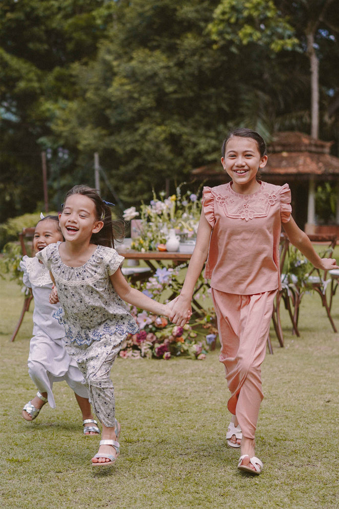 Sisters playing around happily in the garden wearing high quality modern clothes by petit moi