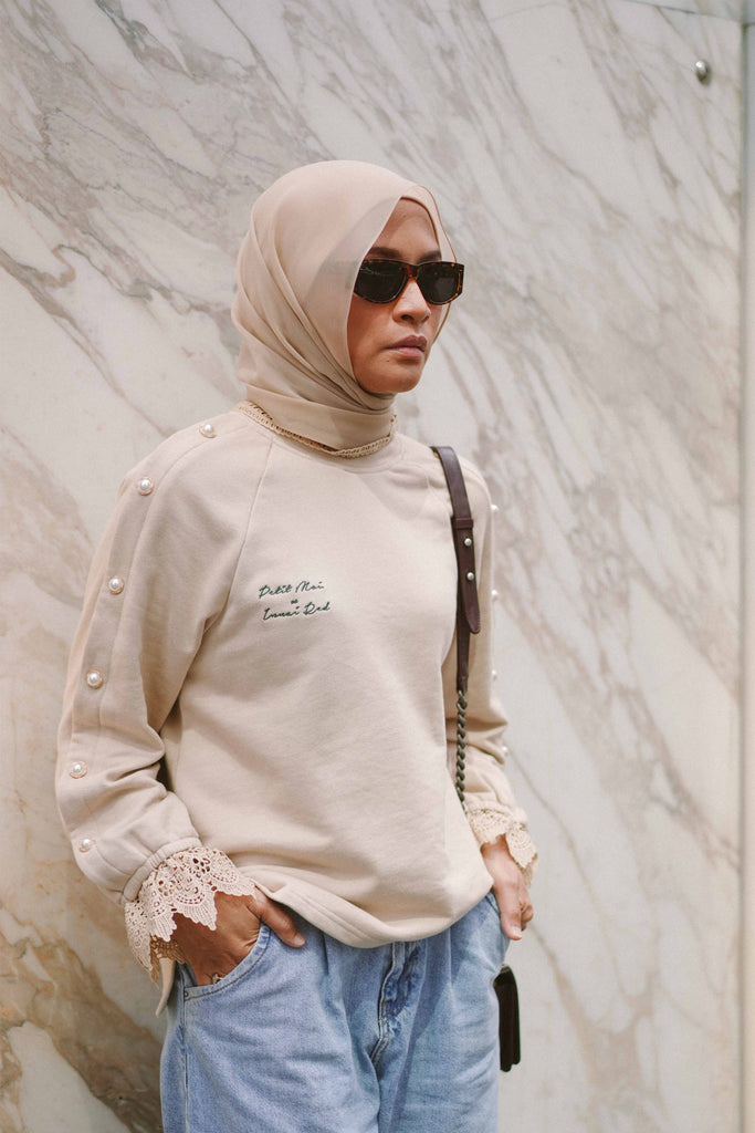 female model wearing sunglasses and a beige jumper posing by a marble wall