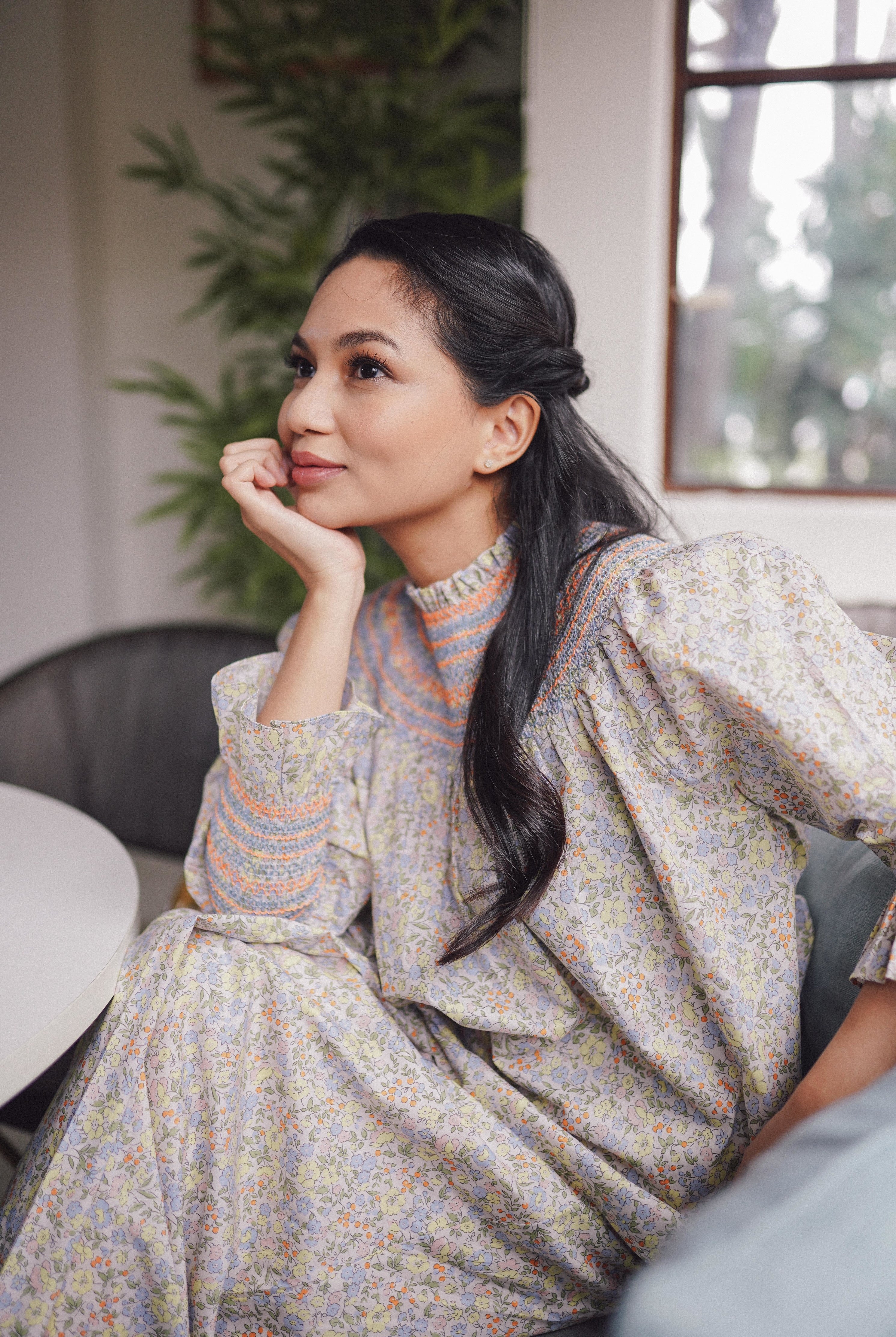 female model in pastel floral baju kurung resting her head on her hand 