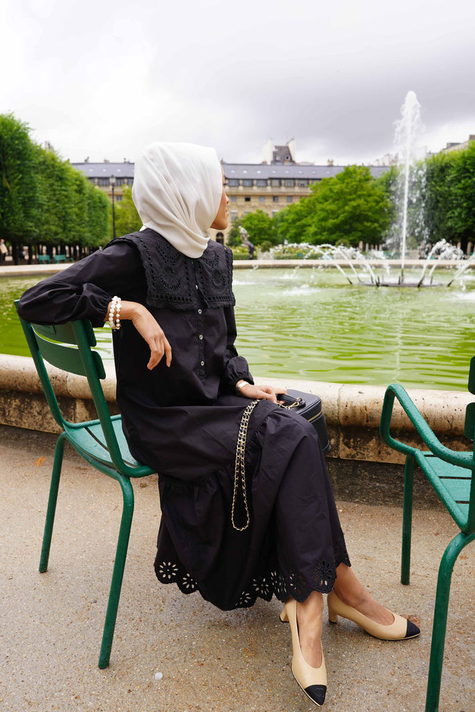 female model in black dress made by petit moi. sitting down on a chair, in paris