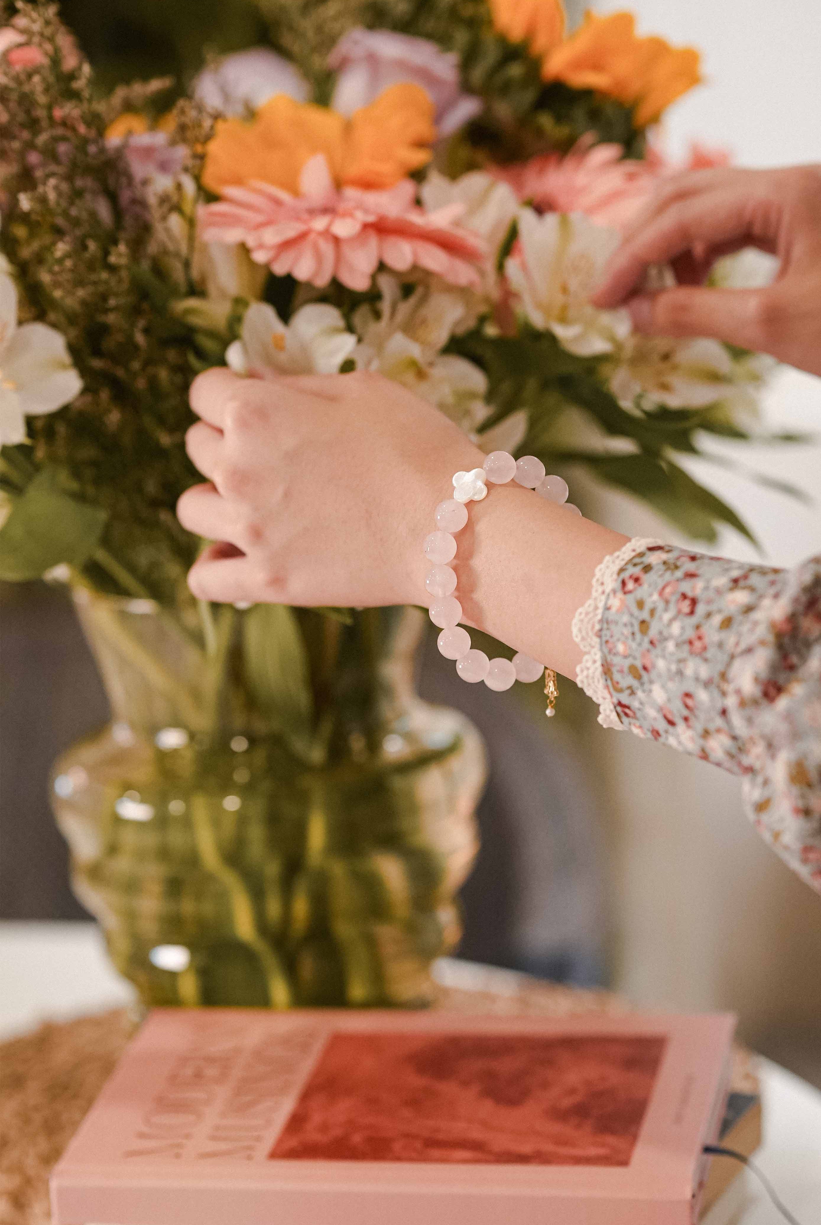 Woman with a white pearl bracelet fluffing up the flowers on the table 