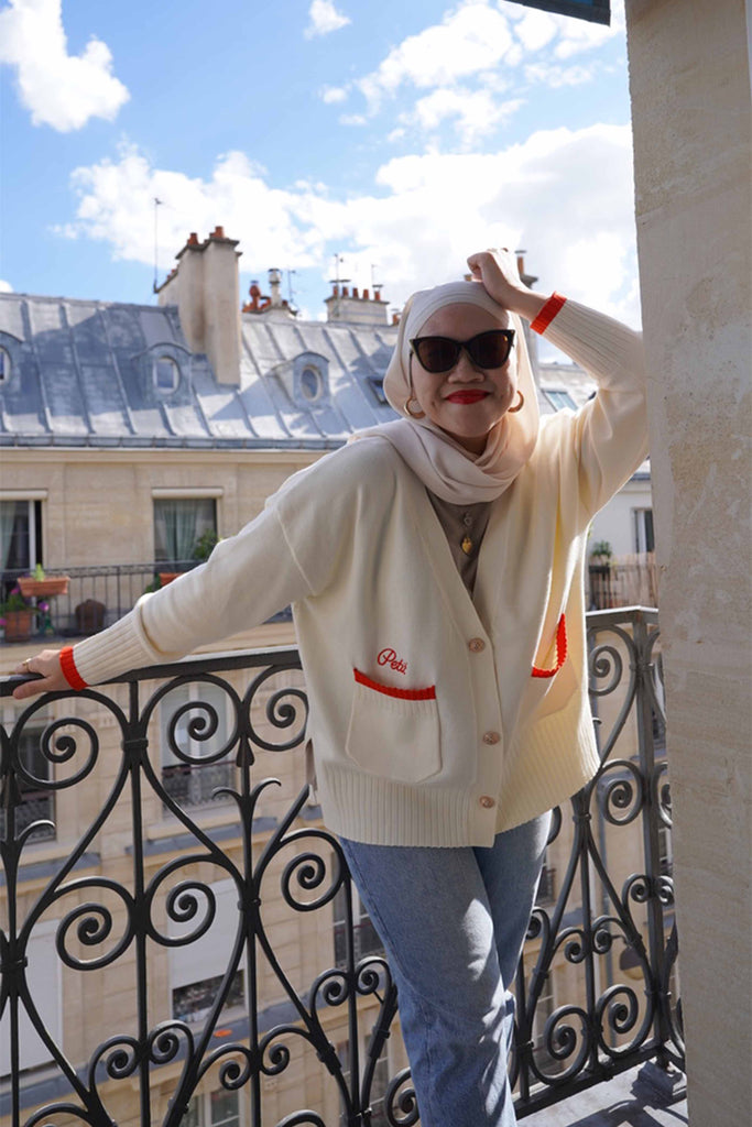 female model posing by the balcony in paris, wearing a high quality cardigan made by petit moi