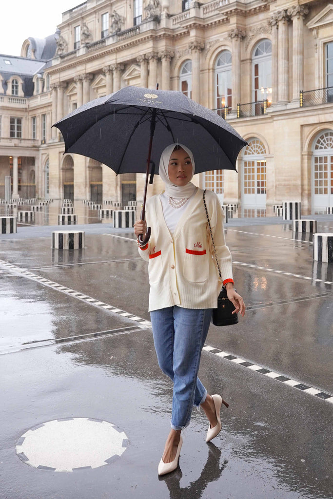woman walking in the rain with an umbrella. whilst wearing a high quality cardigan made by petit moi