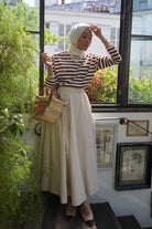 Female model wearing high quality striped brown blouse and skirt by petit moi. Posing with an aesthetic background