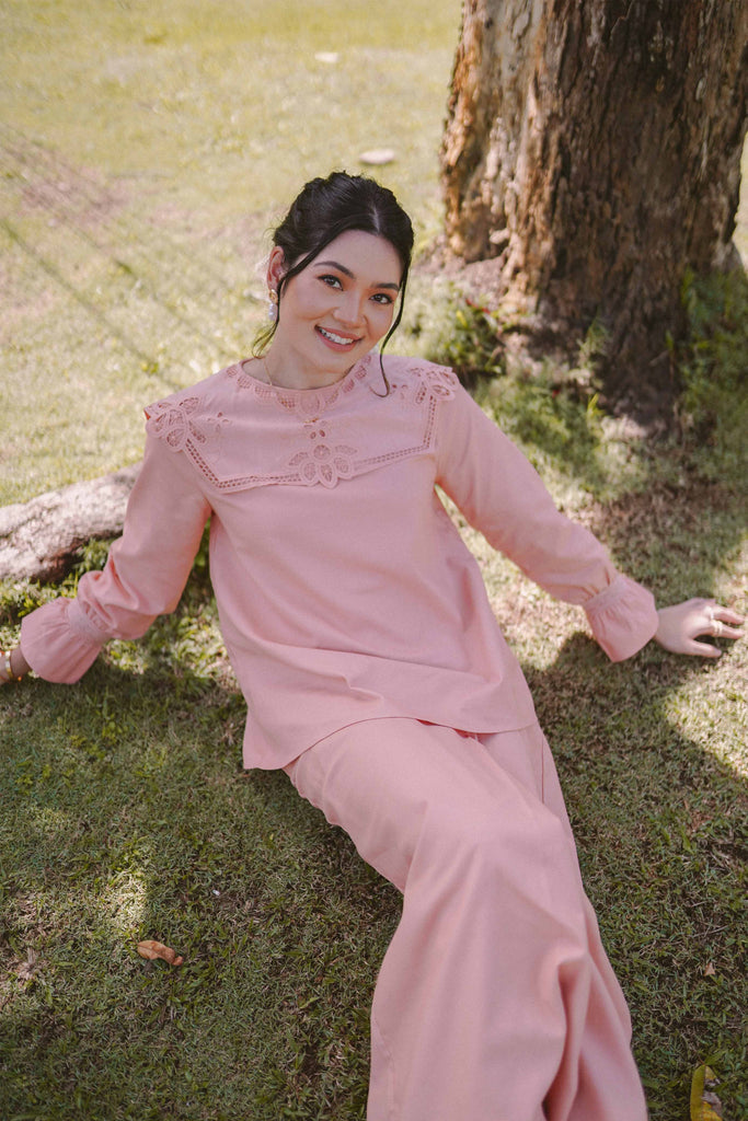 Female model sitting down by the tree and posing for the camera in pink baju kurung